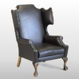 A Queen Anne style brown upholstered and studded wing back armchair,