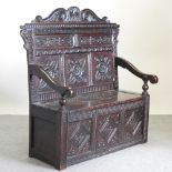 A 19th century heavily carved dark oak box settle, with a scrolled panelled back,