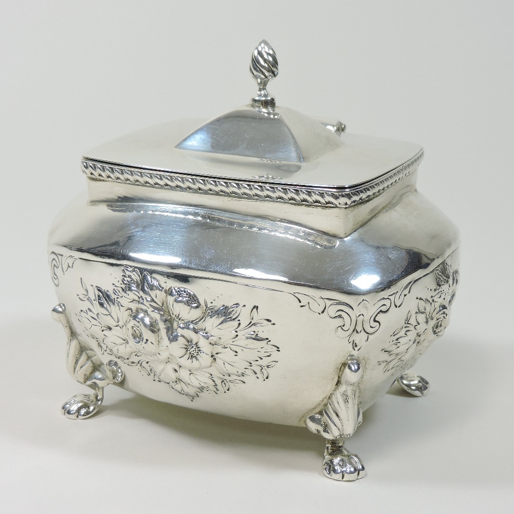 An early 20th century silver tea caddy, relief decorated with flowers, on paw feet,