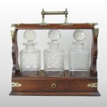 An early 20th century oak and metal mounted tantalus, containing three glass decanters and stoppers,