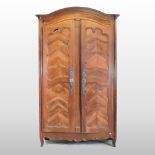 An 18th century French walnut armoire, with a shaped top, enclosed by a pair of panelled doors,