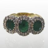An 18 carat gold emerald and diamond halo ring, set with three emeralds,