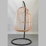 A wicker hanging egg shaped chair, on a metal frame,