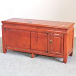 A Tibetan red lacquered cabinet, with a hinged top, enclosed by a panelled door,