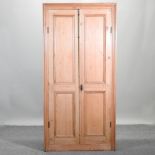 An antique pine cabinet, enclosed by panelled doors,