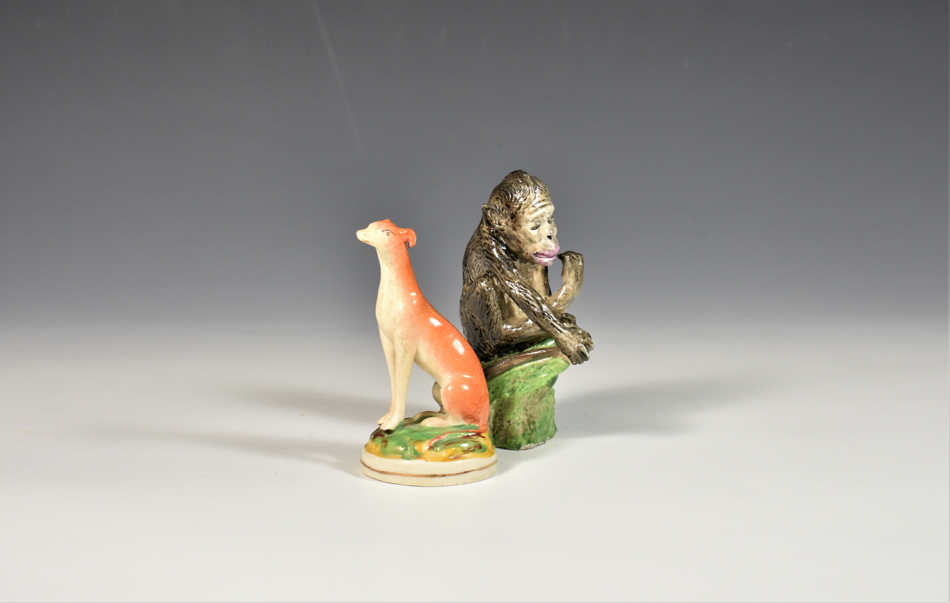 A late 19th century porcelain chimpanzee together with a Staffordshire greyhound (2)