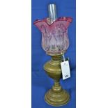 An Antique brass oil lamp with etched ruby glass floral decorated shade.