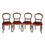 A set of four Victorian walnut balloon-back dining chairs with floral carving to the centre, over