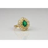 An 18ct gold, emerald and diamond cluster ring the oval cut emerald within a two tier ballerina