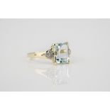 A 9ct gold, aquamarine and diamond ring the emerald cut aquamarine over split shoulders, each set