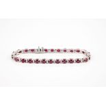 An 18ct white gold, ruby and diamond line bracelet the twenty six oval cut rubies divided by pairs