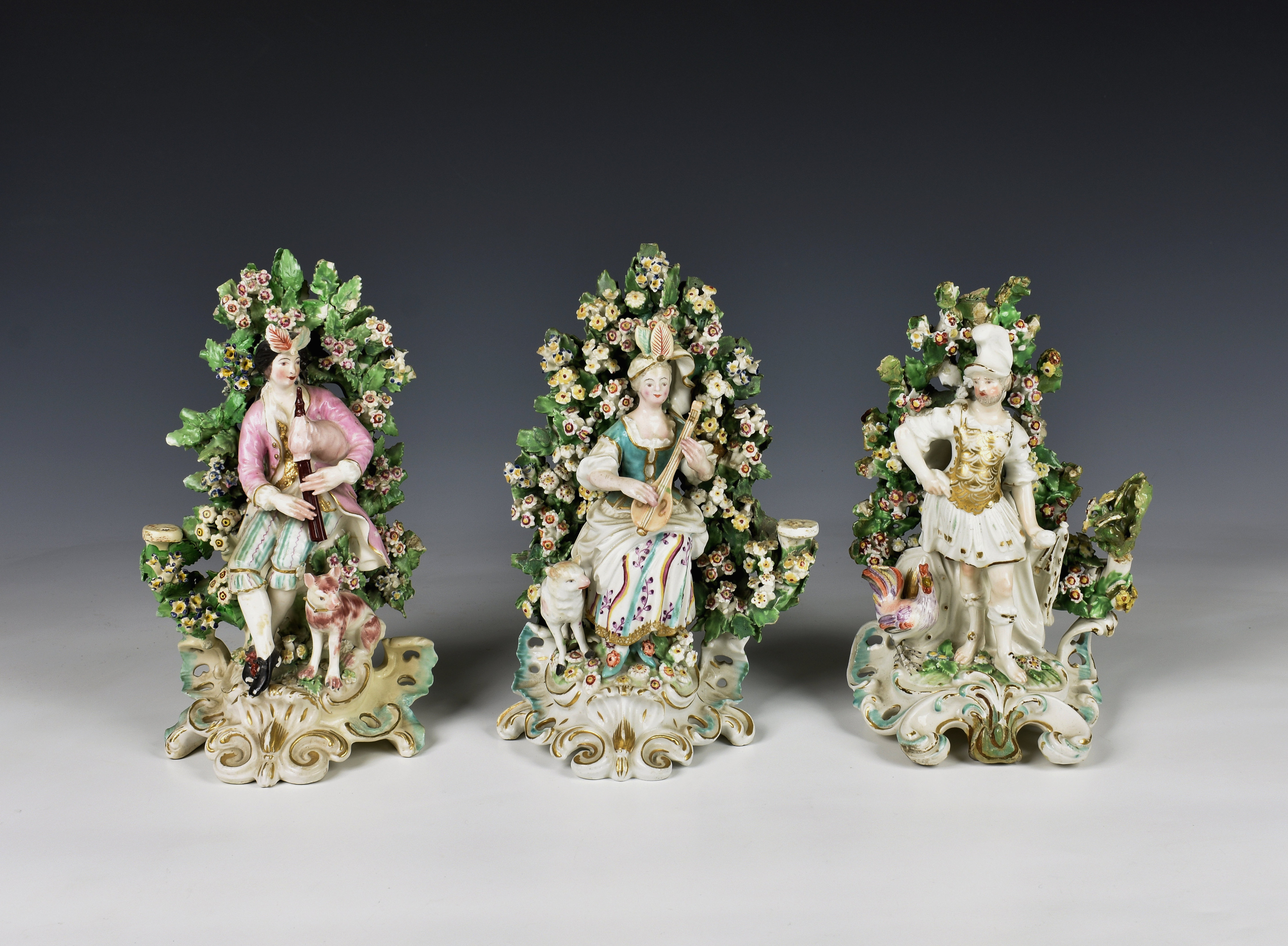 A pair of Derby porcelain seated bocage figures late 18th century, of a piper with dog and a