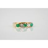 A 9ct gold, emerald and diamond ring with three round cut emeralds divided by two eight cut