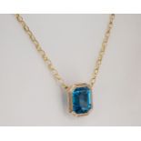 A 9ct gold and blue stone pendant the emerald cut stone within a matted and polished bevel edged