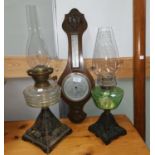 Two Victorian cast iron and glass oil lamps; an aneroid barometer with thermometer