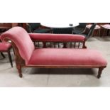 An Edwardian stained frame chaise longue on turned legs, upholstered in pink dralon