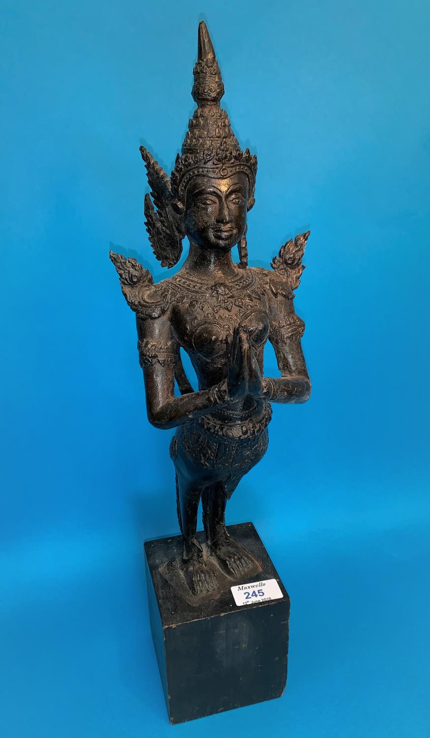 A Thai bronze figure of a goddess with hands folded in prayer and long tail on wooden plinth, height