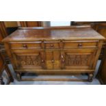 A golden oak sideboard in the "Cotswold School" style with 3 frieze drawers, 2 carved cupboards