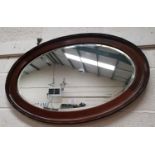 An oval bevelled edge wall mirror in beaded mahogany frame