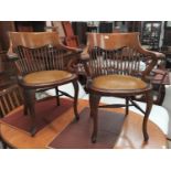 A pair of early 20th century oak stick back smokers bow arm chairs with studded tan coloured seats