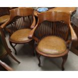 A pair of early 20th century oak stick back smokers bow arm chairs with studded tan coloured seats