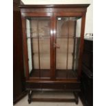 A 1930's oak 2 door china cabinet with lower drawer and blind fret frieze, on barley twist legs