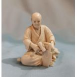A Japanese early 20th century carved Ivory miniature Okimono figure of a man seated with tools,