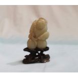 A Chinese jade coloured hardstone carving depicting a seated figure, height 2", on hardwood base