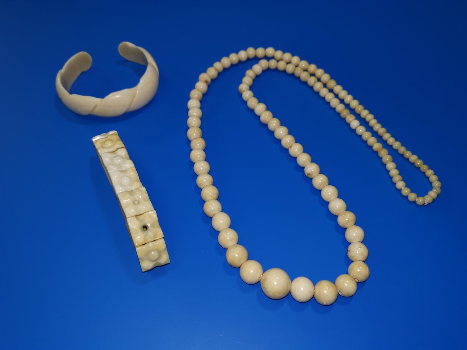 A string of antique ivory graduated beads, 28"; a plaque bracelet; a bangle