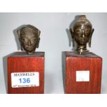 Two South East Asian Buddha heads in gilt bronze, mounted on hardwood columns, 6 cm x 5 cm (1 a.f.)