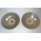 A near matching pair of shallow stoneware bowls, grey with part celadon glaze, on raised foot