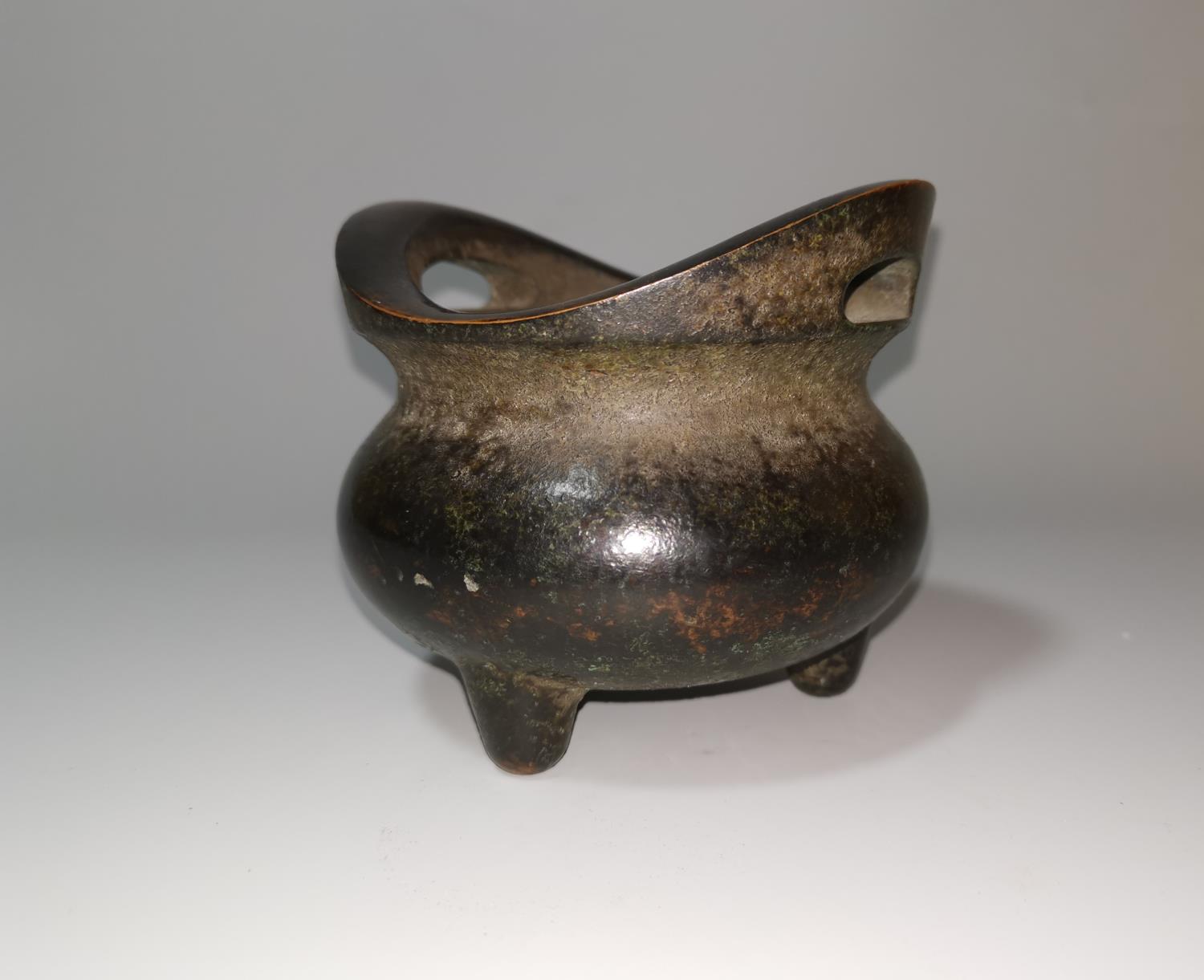A Chinese patinated bronze incense burner of squat tripod form, flattened loop handles, 12 cm