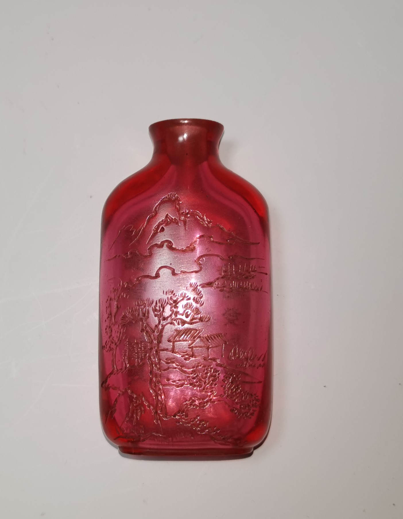 A Chinese ruby coloured glass snuff bottle engraved with landscapes to one side, 28 character text