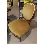 A Victorian walnut low seat nursing chair with oval carved back, upholstered in gold