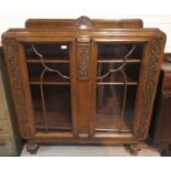 A 1930's golden oak display cabinet with carved decoration, enclosed by 2 doors