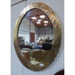 An Arts and Crafts style oval wall mirror with hammered brass frame. 28¼' high