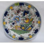 A Delftware charger painted with flowers and a bridge in shades of green, blue, iron red, ochre