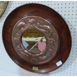 An Arts and Crafts mahogany circular looking glass with Newlyn copper inset, repousse decorated with