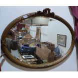 A Victorian gilt gesso oval wall mirror with ribbon-tie reeded frame and foliate surmount, the