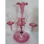 A Victorian cranberry glass epergne, hung with two glass baskets on scrolled clear glass cane