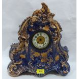 An early 20th century ceramic mantle timepiece, the rococo revival case gilded and blue glazed.