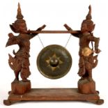 A SOUTH EAST ASIAN CARVED HARDWOOD DINNER GONG, FLANKED BY A PAIR OF GUARDIANS, 50 X 50CM, A SOUTH