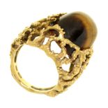 A TIGER EYE RING, THE HIGH DOMED CABOCHON REVERSE SET IN TEXTURED OPENWORK GOLD MOUNT, MARKED 750,