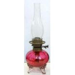 A VICTORIAN GLOBULAR CRANBERRY GLASS OIL LAMP ON THREE CLEAR FEET, WITH BRASS BURNER, 22CM H