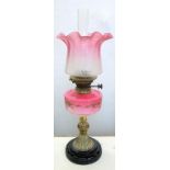 A VICTORIAN ENAMELLED SHADED PINK CASED GLASS AND BRASS MOUNTED OIL LAMP ON BLACK GLAZED EARTHENWARE