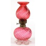 A VICTORIAN SPIRALLY REEDED CRANBERRY GLASS OIL LAMP AND SHADE, THE GLOBULAR RESERVOIR ON FIVE CLEAR