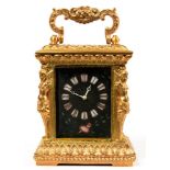 AN ORNATE GILTMETAL MINIATURE CARRIAGE TIMEPIECE WITH ENAMEL MASK DIAL, 8.5CM H EXCLUDING HANDLE,