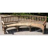 A CURVED TEAK GARDEN SEAT with slightly dished, slatted seat, 99cm h, 300cm l++Weathered but