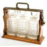 AN EDWARDIAN EPNS MOUNTED OAK TANTALUS, 34CM L AND THREE MOULDED GLASS DECANTERS AND STOPPERS, EARLY