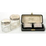 A PAIR OF GEORGE V SILVER NAPKIN RINGS, BIRMINGHAM 1933, CASED AND TWO SILVER TOPPED GLASS JARS,